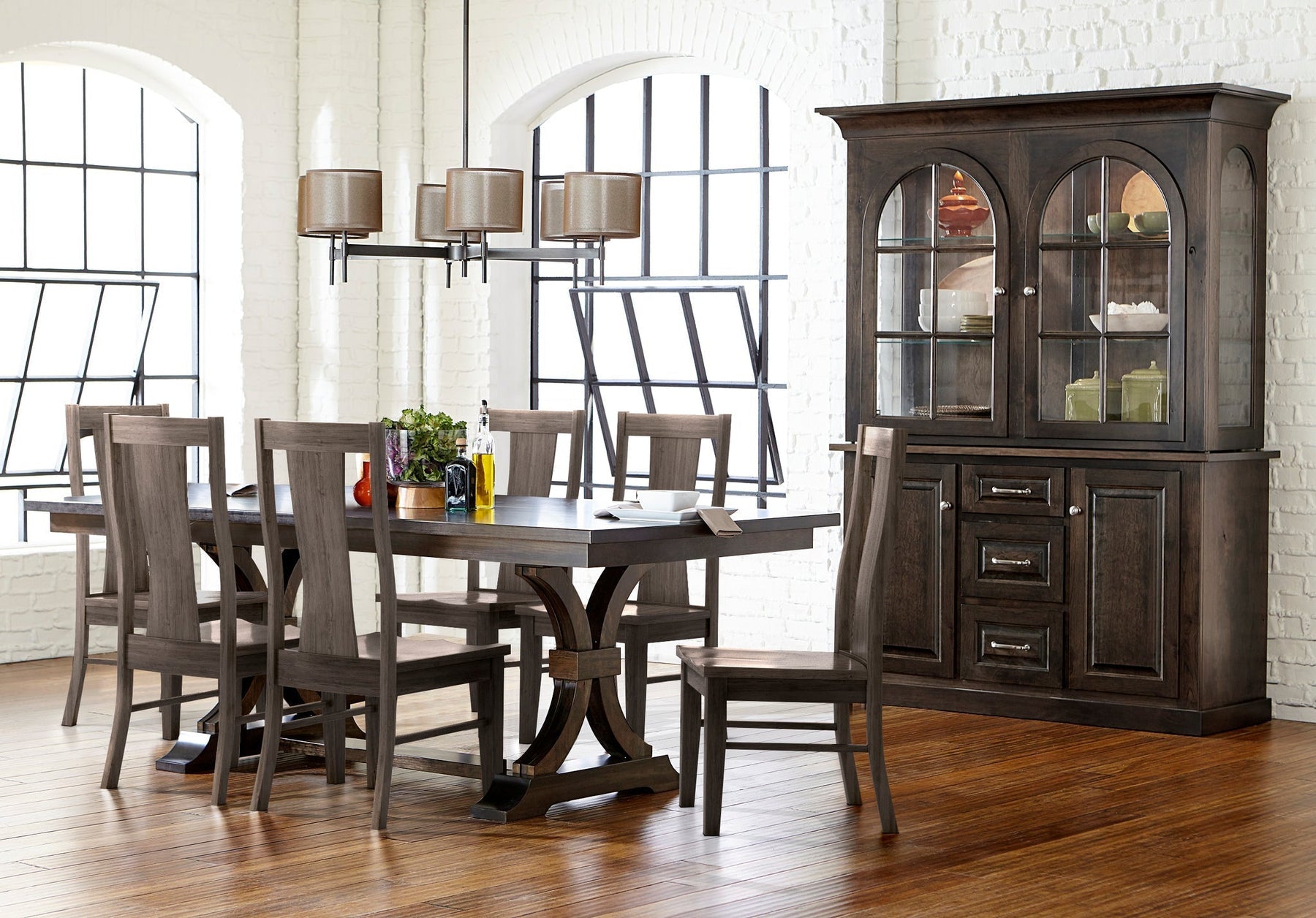 A Fusion custom dining set in a dark stained finish, with a trestle table on a curved double-pedestal base, six tall-back side chairs, and a matching hutch with arched glass doors